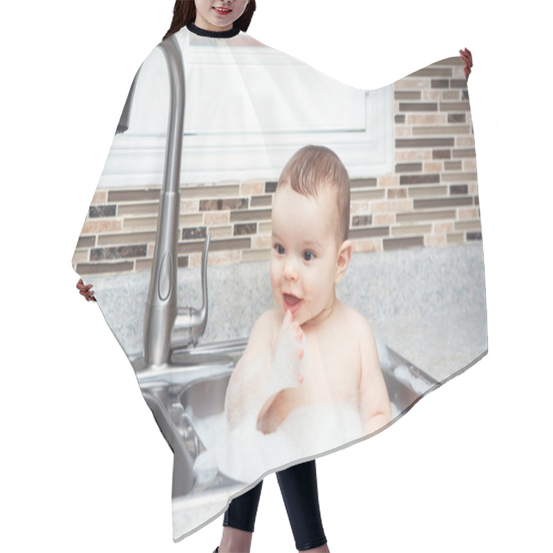 Personality  Portrait Of Cute Caucasian Funny Baby Girl Boy With Dark Black Eyes Sitting In Big Kitchen Sink With Water And Foam  Near Window Looking Away, Lifestyle Everyday Concept Hair Cutting Cape