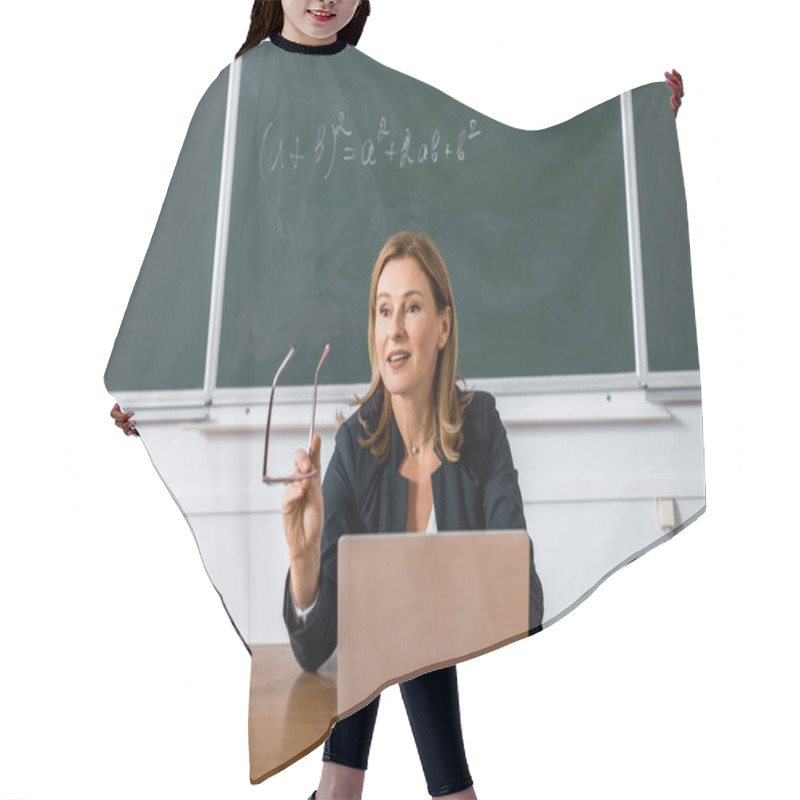 Personality  Female Teacher Sitting At Computer Desk, Holding Glasses And Talking In Classroom  Hair Cutting Cape