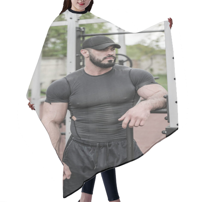 Personality  Handsome Young Bearded Male In Black Sportswear And Cap Standing Lean On Street Outdoor Gym Equipment Hair Cutting Cape