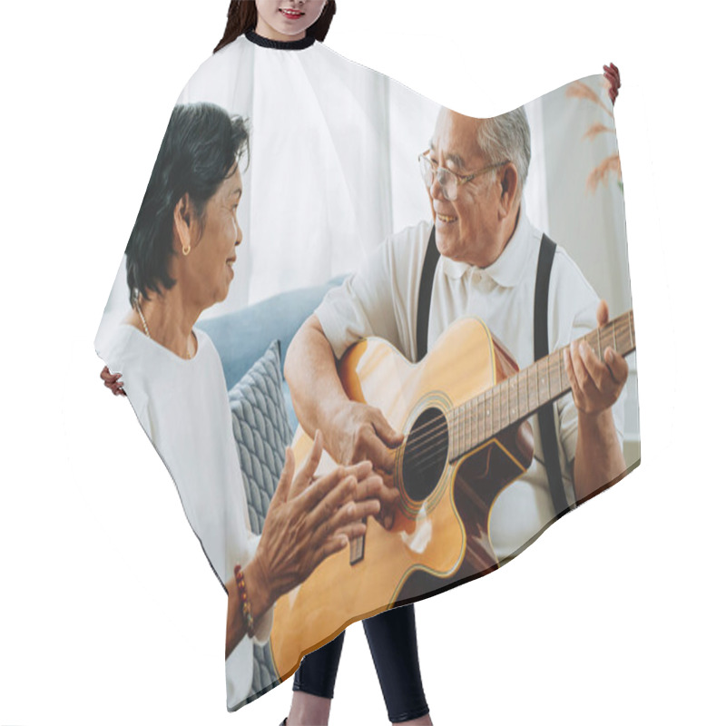 Personality  Asian Senior Couple Sitting On The Sofa And Playing Acoustic Guitar Together. Happy Smiling Elderly Woman Clapping Hands While Old 70s Guitarist Husband Singing. Enjoying Retirement Life At Home. Hair Cutting Cape