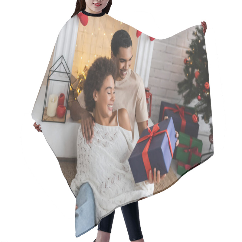 Personality  Joyful African American Couple With Christmas Present Sitting On Floor Near Fireplace  Hair Cutting Cape