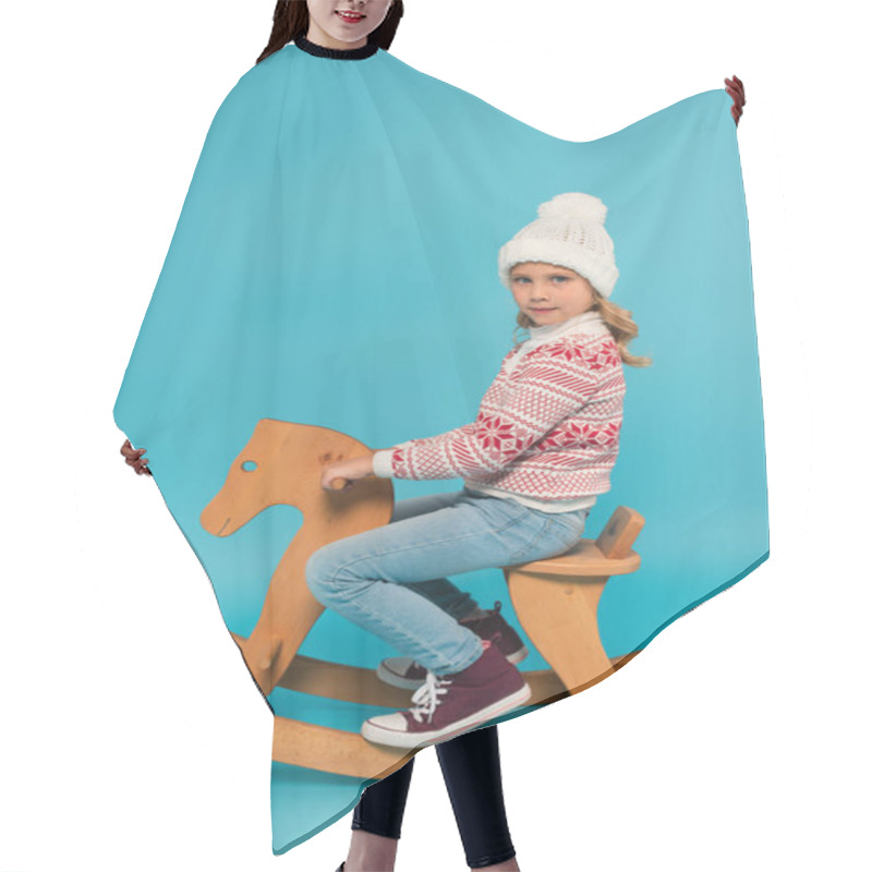 Personality  Girl In Warm Hat And Sweater Riding Rocking Horse While Looking At Camera On Blue Hair Cutting Cape