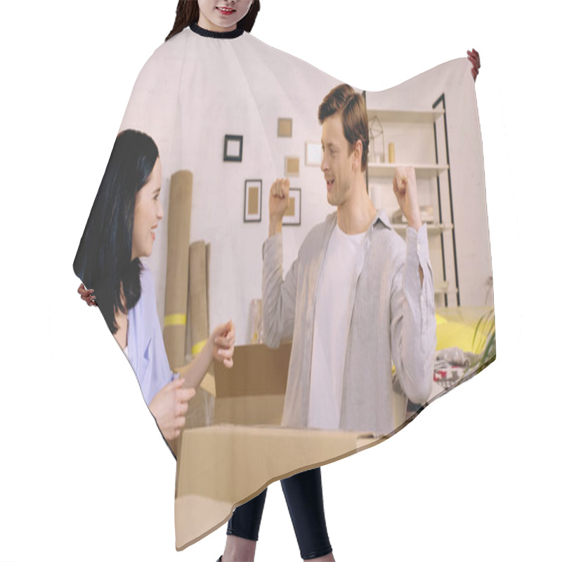 Personality  Happy Woman Looking At Boyfriend Showing Muscles Near Carton Boxes Hair Cutting Cape