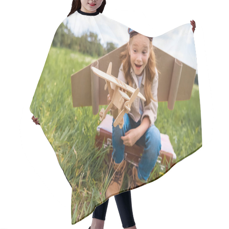 Personality  Emotional Kid In Pilot Costume With Wooden Toy Plane In Hand Sitting On Retro Suitcase In Field Hair Cutting Cape