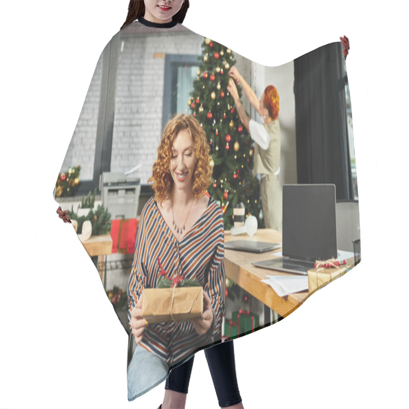 Personality  Young Woman With Gift With Her Colleague Decorating Christmas Tree On Backdrop. Hair Cutting Cape