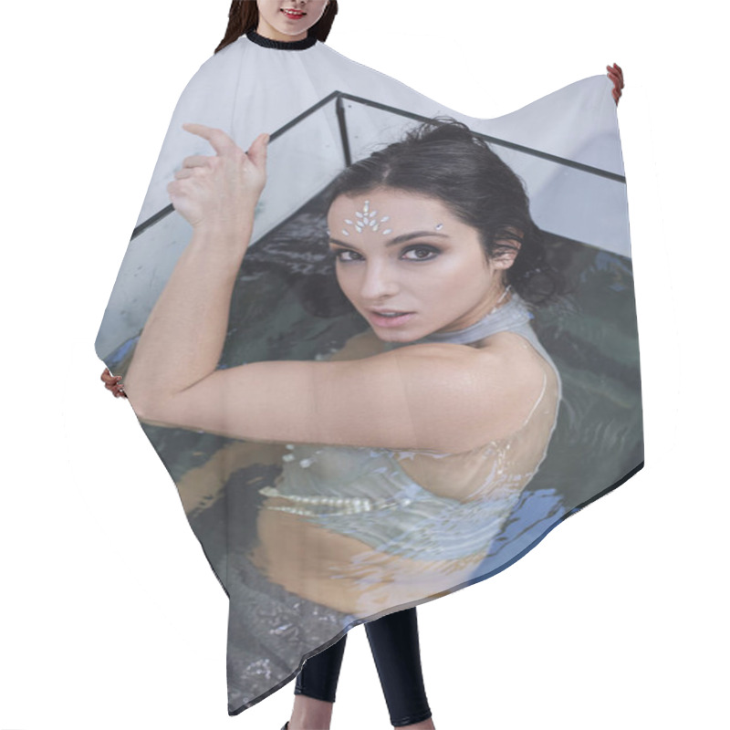 Personality  A Young Woman With Dark Hair And Glittering Face Paint Poses In An Aquarium, Looking Up At The Camera. Hair Cutting Cape