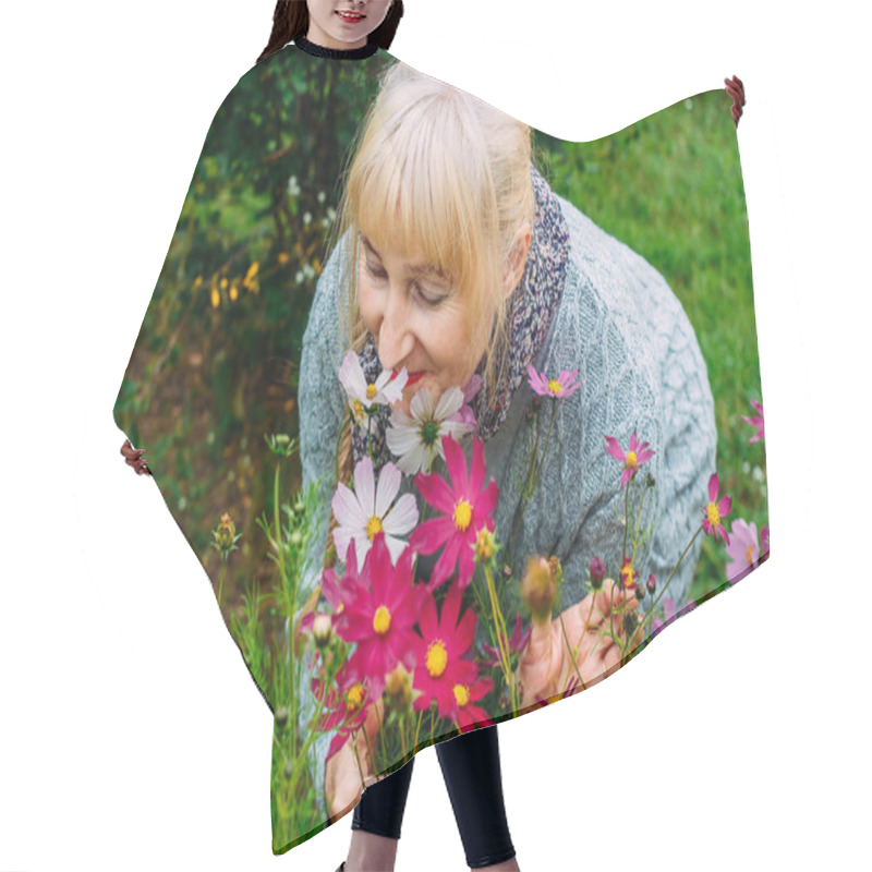 Personality  Attractive Blonde Woman Pensioner In A Gray Cardigan Sniffs Blooming Cosmos In The Summer In The Garden Hair Cutting Cape