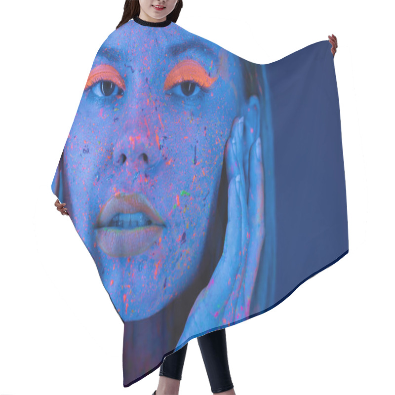 Personality  Portrait Of Woman In Vibrant Neon Makeup And Body Paint Touching Face And Looking At Camera Isolated On Dark Blue Hair Cutting Cape