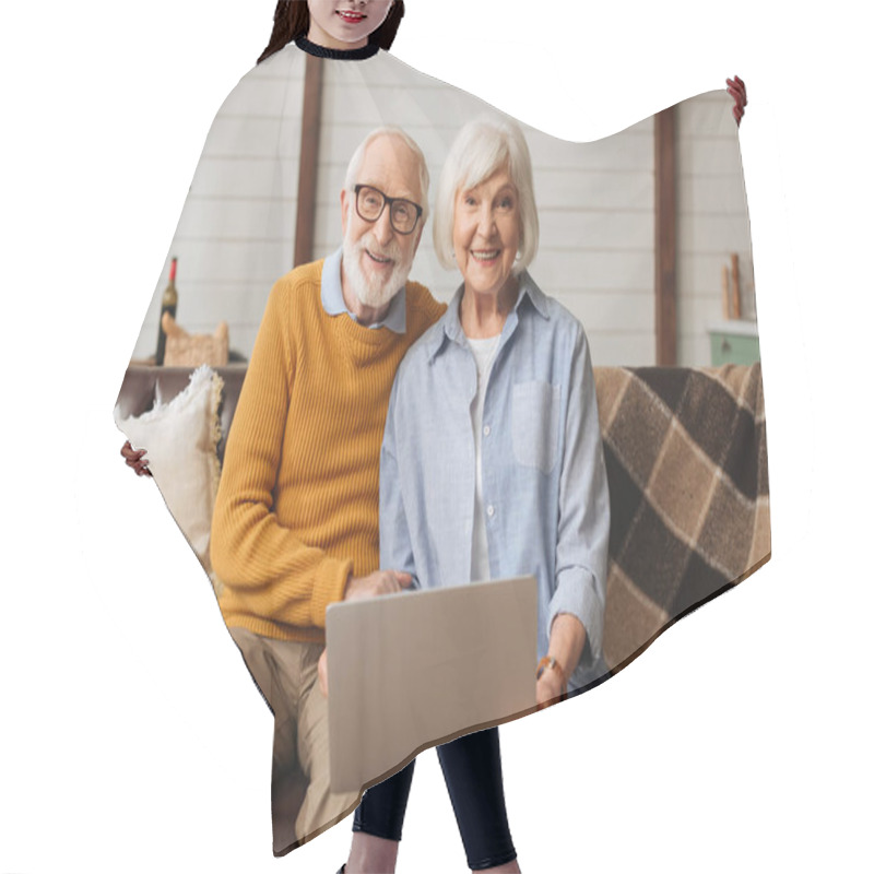 Personality  Cheerful Elderly Husband Hugging Wife With Laptop While Looking At Camera On Couch In Living Room On Blurred Background Hair Cutting Cape