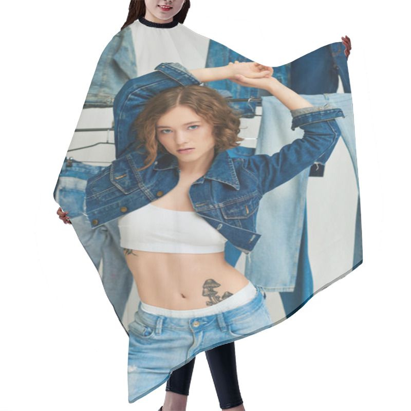 Personality  Tattooed Model In Cropped Jacket And Jeans Posing With Hands Over Head Among Denim Clothes On Gray Hair Cutting Cape