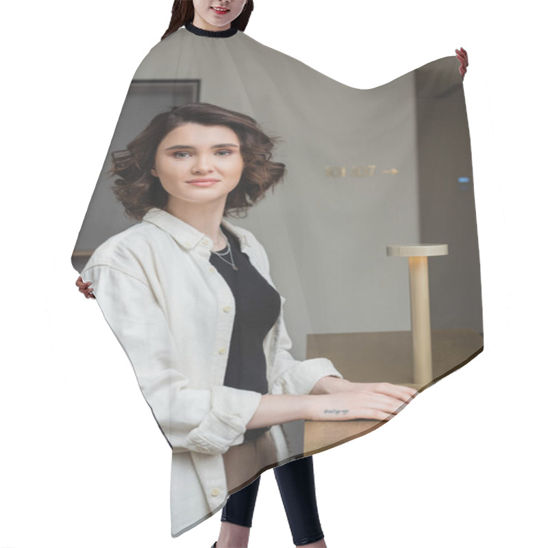 Personality  Young And Joyful Woman With Wavy Brunette Hair, In Trendy Casual Clothes, White Shirt And Black Crop Top Looking At Camera Near Reception Desk And Lamp In Lobby Of Contemporary Hotel Hair Cutting Cape