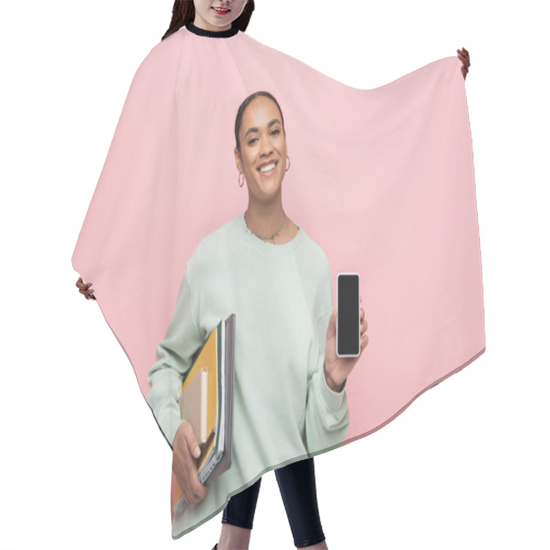 Personality  Smiling African American Student In Sweatshirt Holding Study Supplies And Smartphone With Blank Screen Isolated On Pink  Hair Cutting Cape