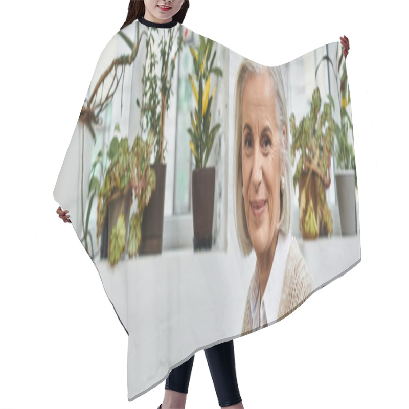 Personality  A Beautiful Woman With Gray Hair Warmly Smiles While Surrounded By Vibrant Greenery Indoors. Hair Cutting Cape