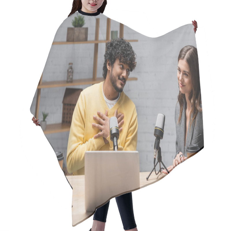 Personality  Honest Indian Podcaster Touching Chest And Looking At Smiling Colleague Near Microphones, Laptop, Takeaway Drinks, Eyeglasses, Notebooks And Smartphones In Broadcasting Studio Hair Cutting Cape