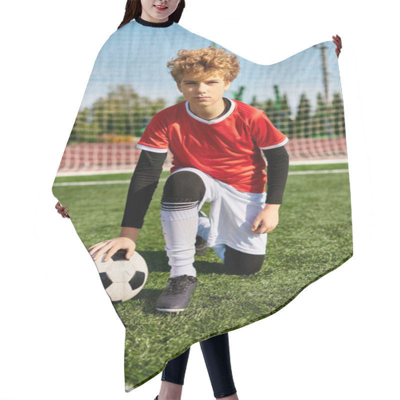 Personality  A Young Boy In A Soccer Uniform Kneels Gracefully On The Grass, Holding A Soccer Ball In Front Of Him. Hair Cutting Cape