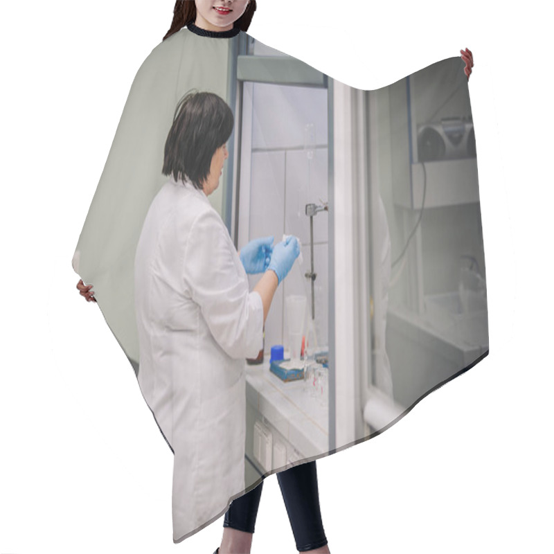 Personality  Valmiera, Latvia - November 18, 2024 - Female Scientist In A Lab Coat Conducting An Experiment In A Laboratory Fume Hood With Glassware And Equipment On The Countertop. Hair Cutting Cape