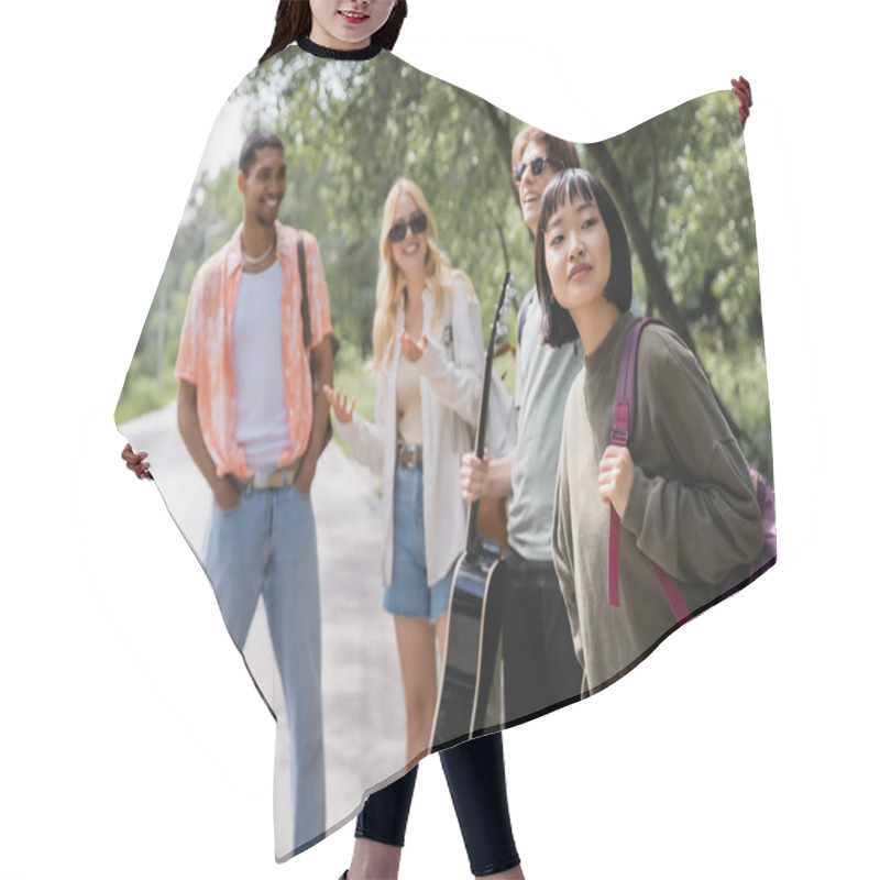 Personality  Asian Woman With Backpack Looking Away Near Blurred Interracial Friends On Road Hair Cutting Cape