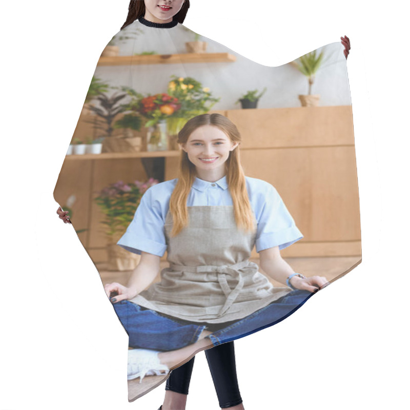 Personality  Beautiful Young Woman In Apron Sitting On Floor And Smiling At Camera In Flower Shop  Hair Cutting Cape