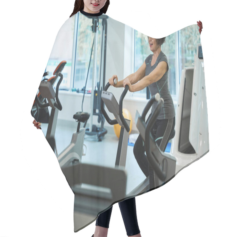 Personality  Smiling Elderly Woman Is Exercising On An Exercise Bike, She Is Undergoing Rehabilitation In A Fitness Clinic Hair Cutting Cape