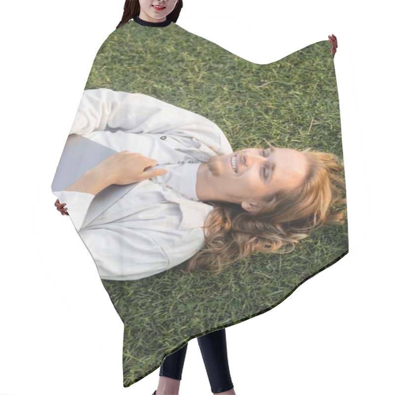 Personality  Top View Of Overjoyed Man With Long Fair Hair Holding Laptop While Lying On Grassy Field Hair Cutting Cape