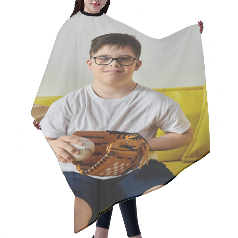 Personality  Adorable Boy With Down Syndrome With Glasses Sitting On A Yellow Couch Holding A Baseball. Hair Cutting Cape