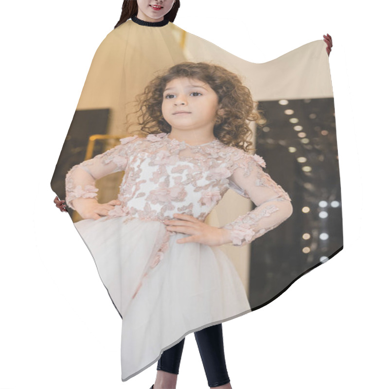 Personality  Curly Middle Eastern And Little Girl In Floral Dress With Tulle Skirt Standing With Hands On Hips And Looking Away In Bridal Boutique, Preparation For Wedding, Blurred Background, Golden Accents Hair Cutting Cape