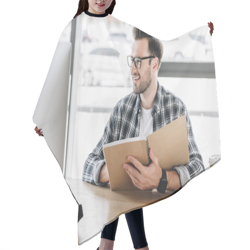 Personality  Smiling Young Man In Eyeglasses Writing In Notebook And Using Desktop Computer At Workplace Hair Cutting Cape