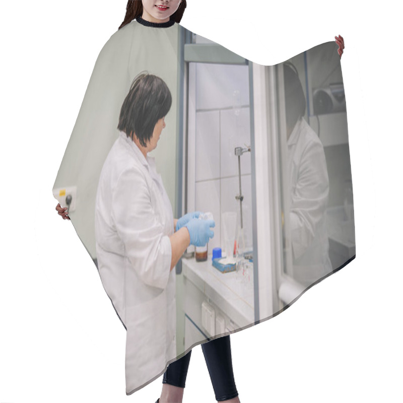 Personality  Valmiera, Latvia - November 18, 2024 - Female Scientist In A Lab Coat Conducting An Experiment In A Laboratory Fume Hood With Glassware And Equipment On The Countertop. Hair Cutting Cape