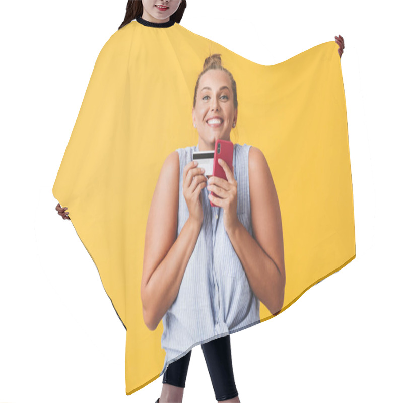 Personality  Young Joyful Woman In Shirt Happily Looking In Camera With Credit Card And Cellphone In Hands Over Yellow Background. Plus Size Model Hair Cutting Cape