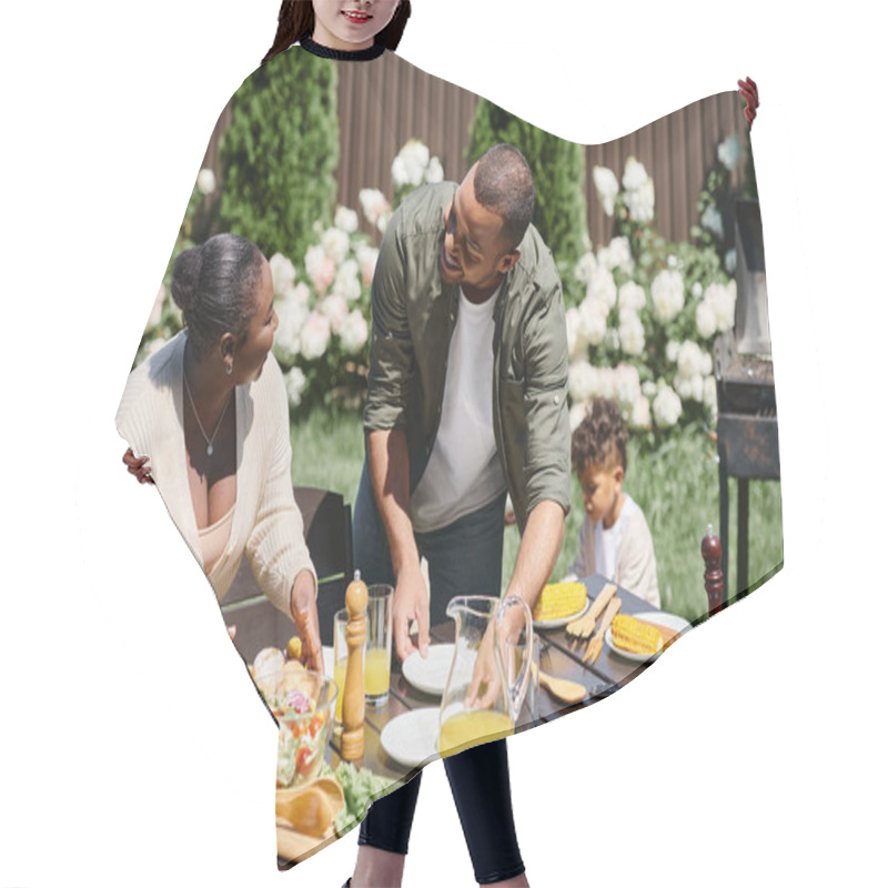 Personality  Cheerful African American Parents Serving Table In Garden Near Son Playing On Backyard, Family Hair Cutting Cape