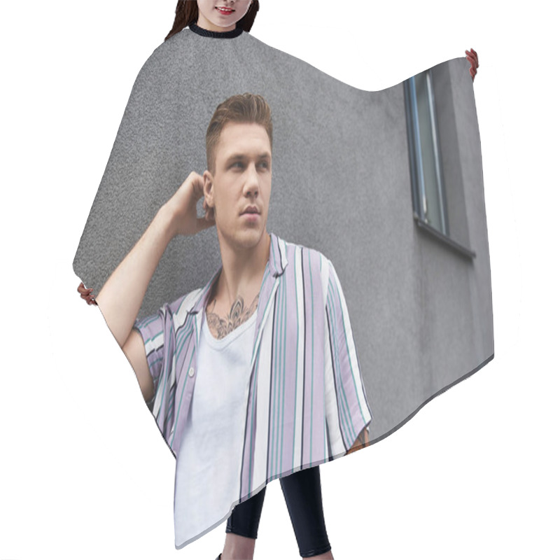 Personality  Young Man With Tattoos Poses Confidently Next To A Textured Gray Wall. Hair Cutting Cape