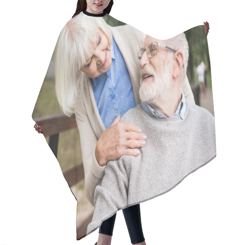 Personality  Smiling Senior Woman Looking At Happy Husband In Wheelchair, While Holding Hand On His Shoulder Hair Cutting Cape