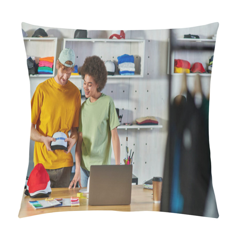 Personality  Smiling Interracial Craftspeople Holding Snapback And Printing Layer While Working On Project Near Laptop And Cloth Samples On Table In Print Studio, Sustainable Business Model Concept Pillow Covers