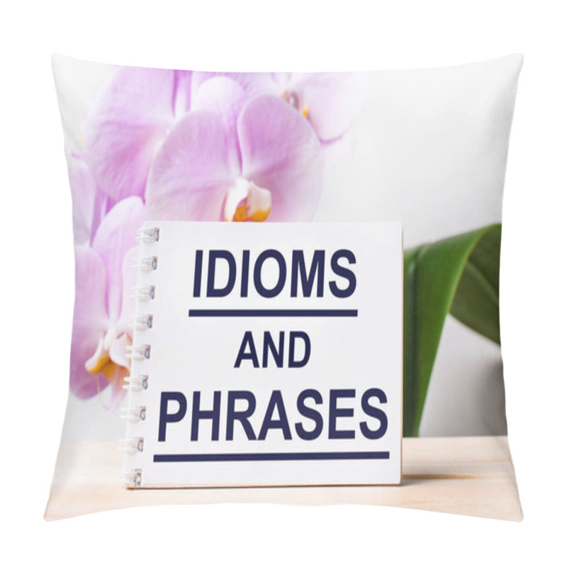 Personality  White Blank Notebook With The Text IDIOMS AND PHRASES On The Table Against The Background Of A Light Pink Orchid. Pillow Covers