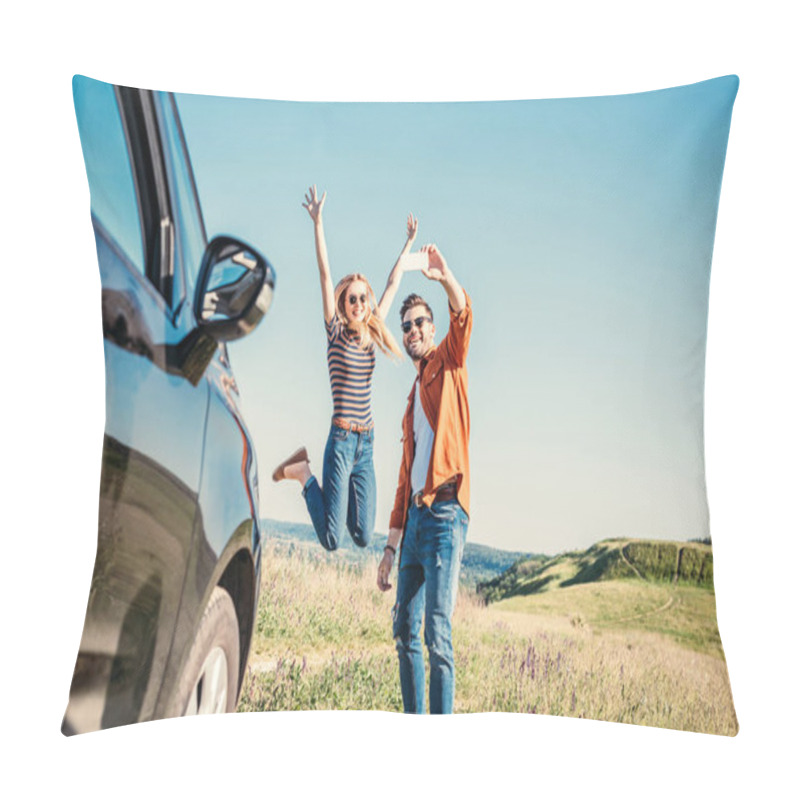 Personality  Happy Young Woman Jumping With Wide Arms While Her Boyfriend Taking Selfie On Smartphone Near Car In Field  Pillow Covers