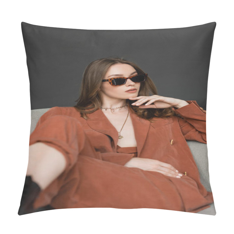 Personality  Stylish Young Woman With Long Hair Wearing Terracotta Suit With Blazer And Pants And Posing In Trendy Sunglasses While Sitting In Comfortable Armchair On Grey Background, Fashionable Model, Look Away Pillow Covers