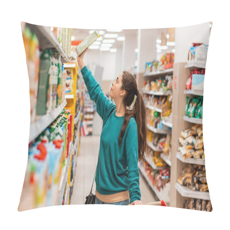 Personality  A Young Pretty Caucasian Woman With A Grocery Cart Pulls A Juice Box From The Top Shelf. The Store Is Blurred In The Background. The Concept Of Buying Goods And Shopping. Pillow Covers