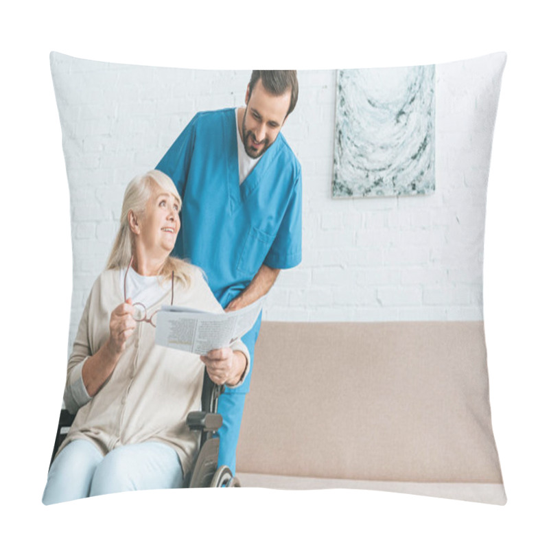 Personality  Smiling Young Male Nurse Looking At Happy Senior Woman Reading Newspaper In Wheelchair  Pillow Covers