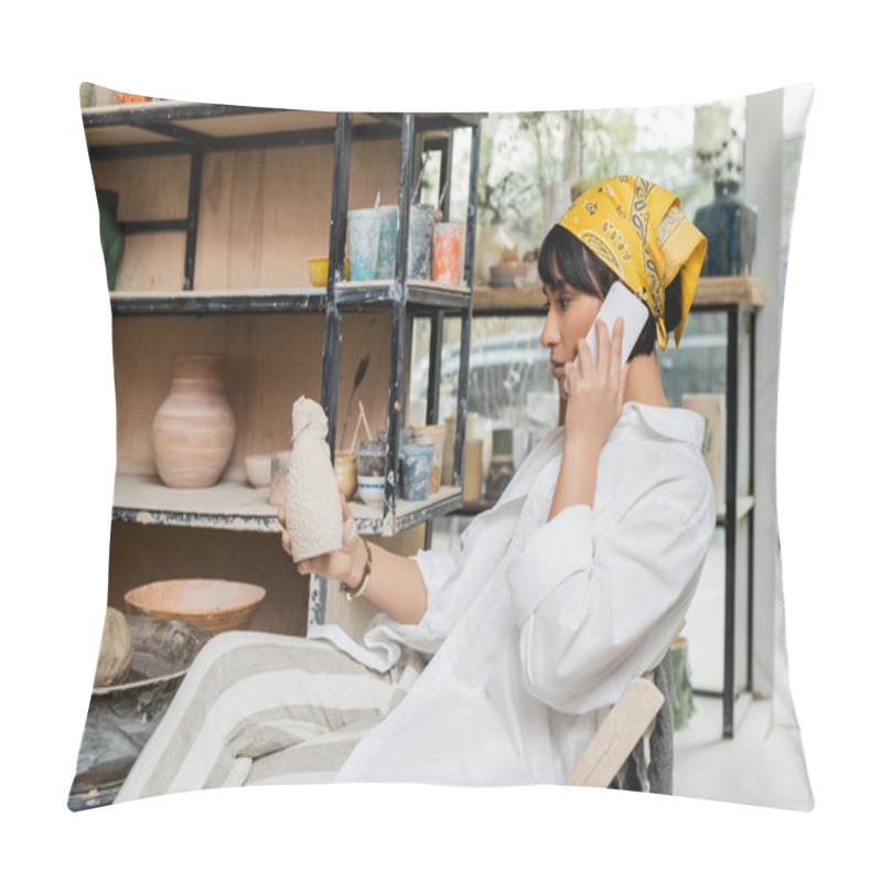 Personality  Side View Of Young Asian Artist In Headscarf And Workwear Talking On Smartphone And Holding Ceramic Sculpture While Sitting In Ceramic Workshop, Artisan In Pottery Studio Focusing On Creation Pillow Covers