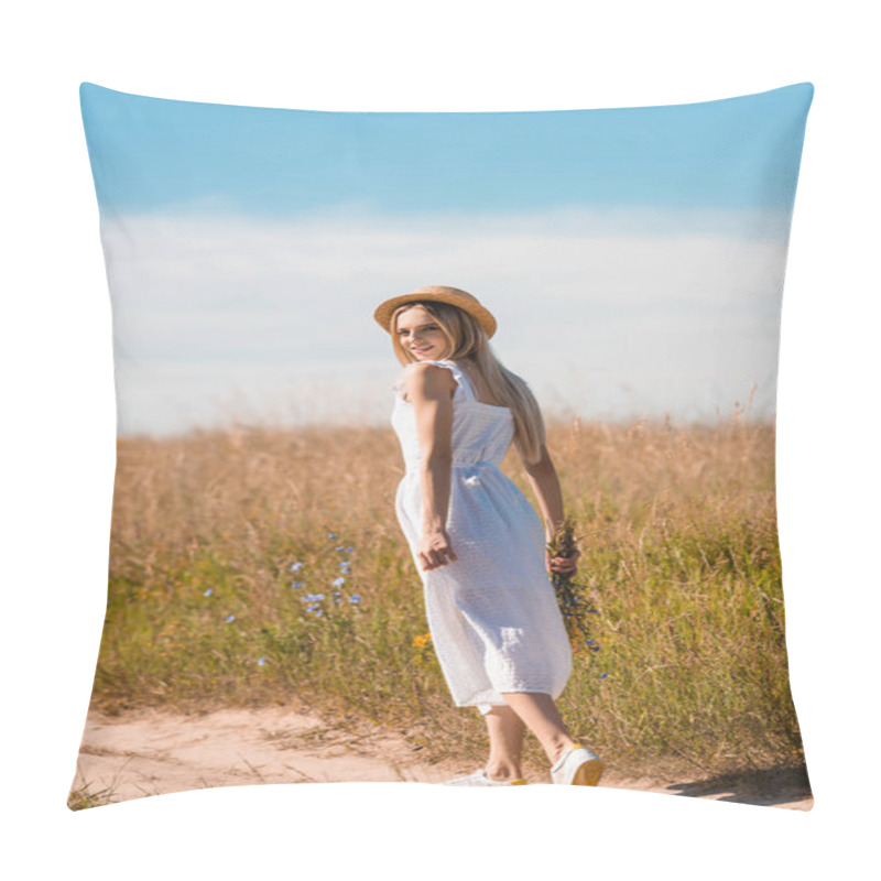 Personality  Young Blonde Woman In Straw Hat And White Dress Holding Wildflowers And Looking At Camera While Walking On Road In Field Pillow Covers