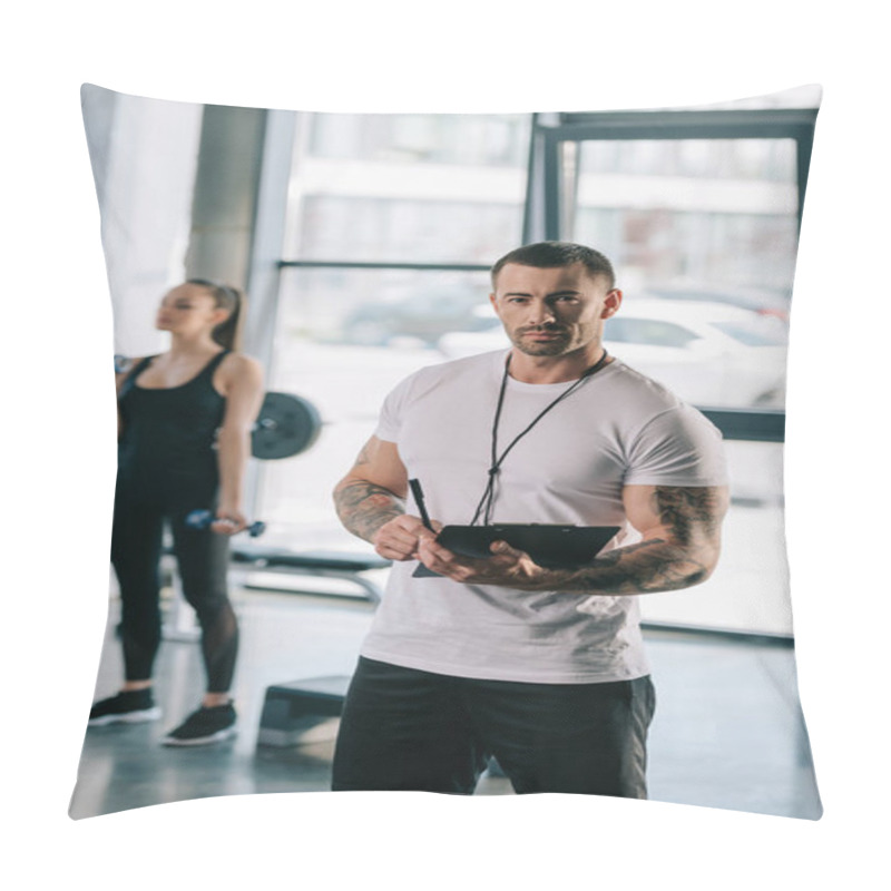 Personality  Personal Trainer With Clipboard And Young Sportswoman Exercising With Dumbbells Behind At Gym Pillow Covers