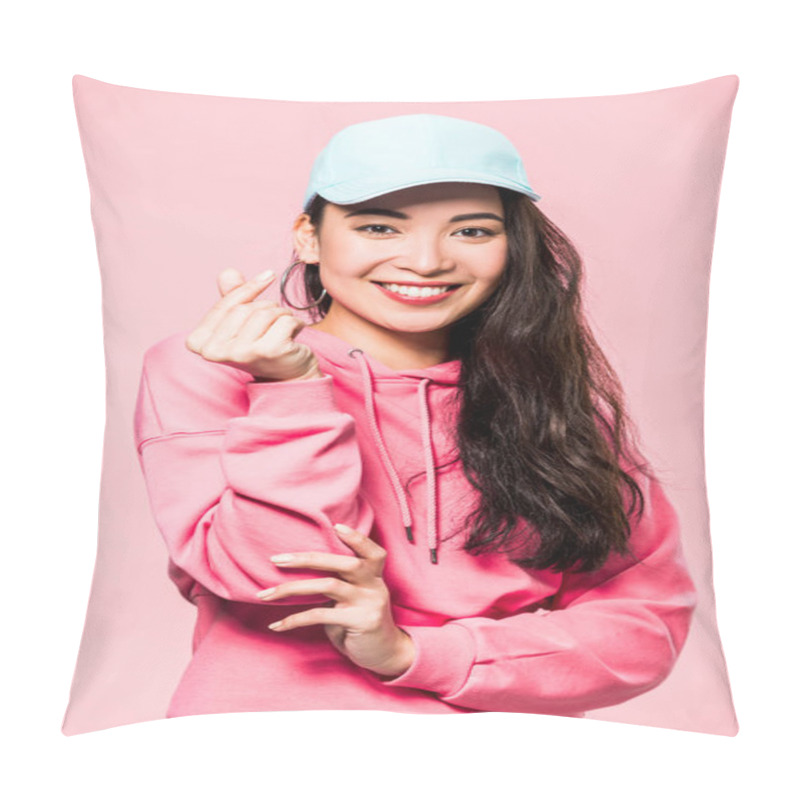 Personality  Attractive Asian Woman In Pink Pullover And Cap Smiling And Showing Heart Symbol Isolated On Pink  Pillow Covers