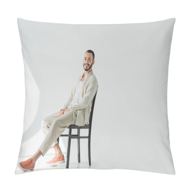 Personality  Positive Brunette Gay Man In Casual Clothes Made Of Natural Fabrics Looking At Camera While Sitting On Comfortable Chair On Grey Background With Sunlight  Pillow Covers