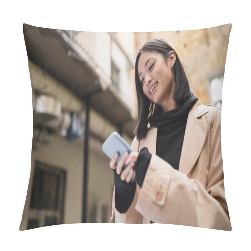 Personality  Low Angle View Of Smiling Asian Woman In Trench Coat Using Smartphone Outdoors  Pillow Covers