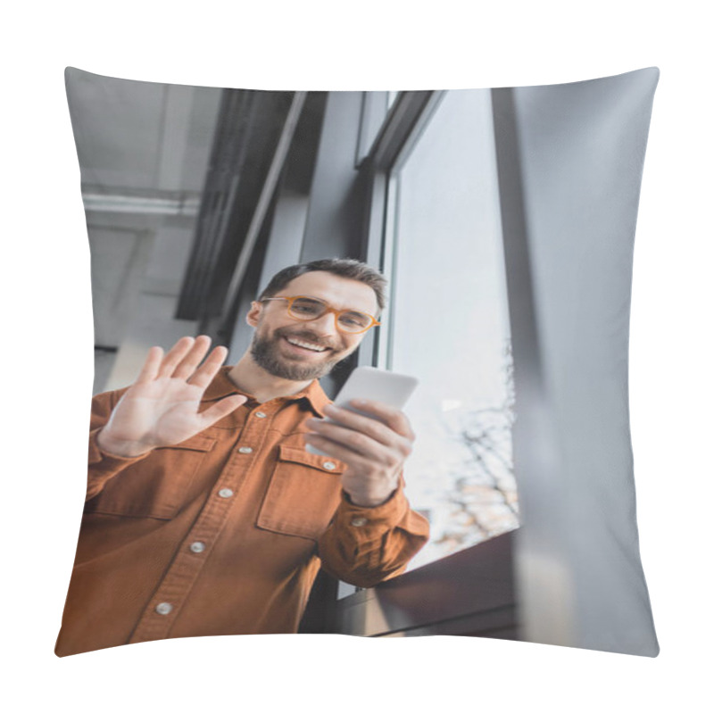 Personality  Low Angle View Of Fashionable And Positive Manager In Shirt And Eyeglasses Holding Mobile Phone And Waving Hand During Video Call Near Window In Office, Blurred Foreground Pillow Covers