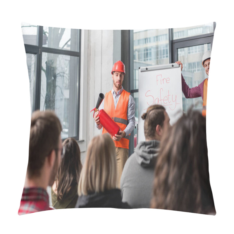 Personality  Selective Focus Of Handsome Fireman In Helmet Holding Extinguisher While Standing Near White Board With Fire Safety Lettering Near Coworker Pillow Covers