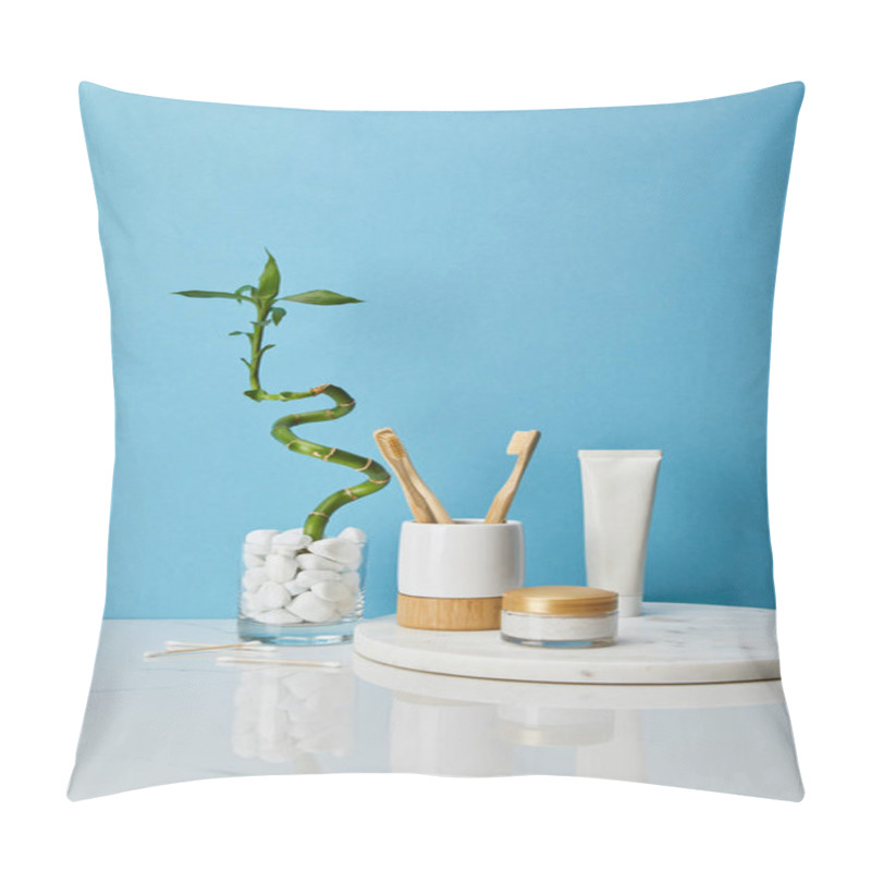 Personality  Toothbrushes In Holder, Cosmetic Cream And Toothpaste In Tube On Round Board Near Green Bamboo Stem In Vase On Blue Background Pillow Covers