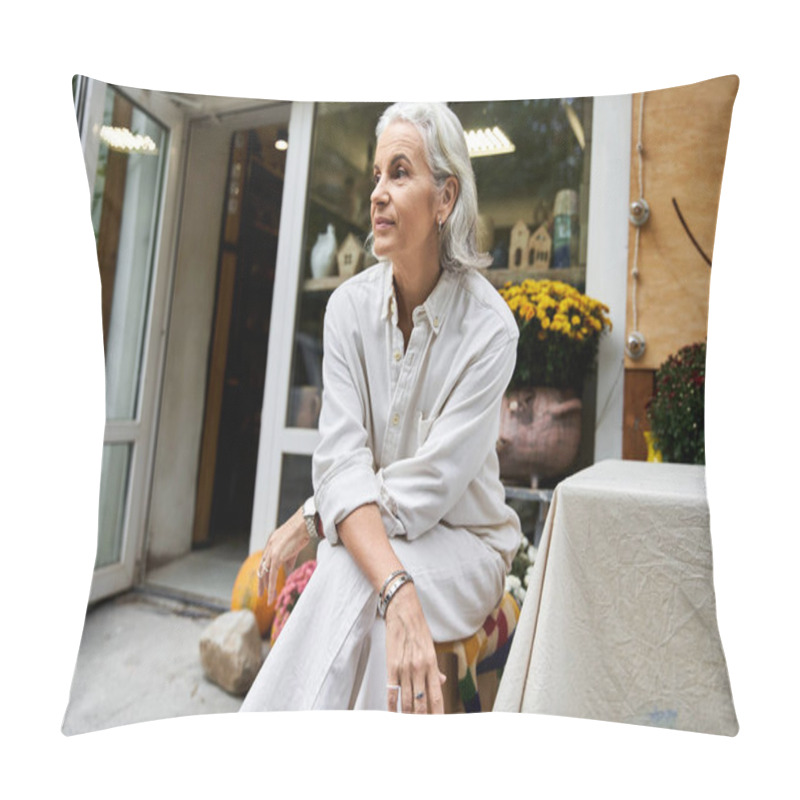 Personality  The Beautiful Mature Woman Sits Thoughtfully Outside A Quaint Shop, Surrounded By Colorful Flowers. Pillow Covers