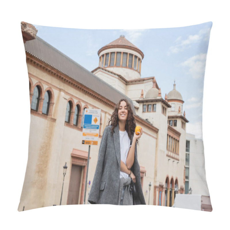 Personality  Cheerful Young And Curly Woman In Casual Warm Jacket Holding Ripe Orange And Leash While Looking At Camera Near Blurred Historical Landmark On Urban Street In Barcelona, Spain, Ancient Building Pillow Covers