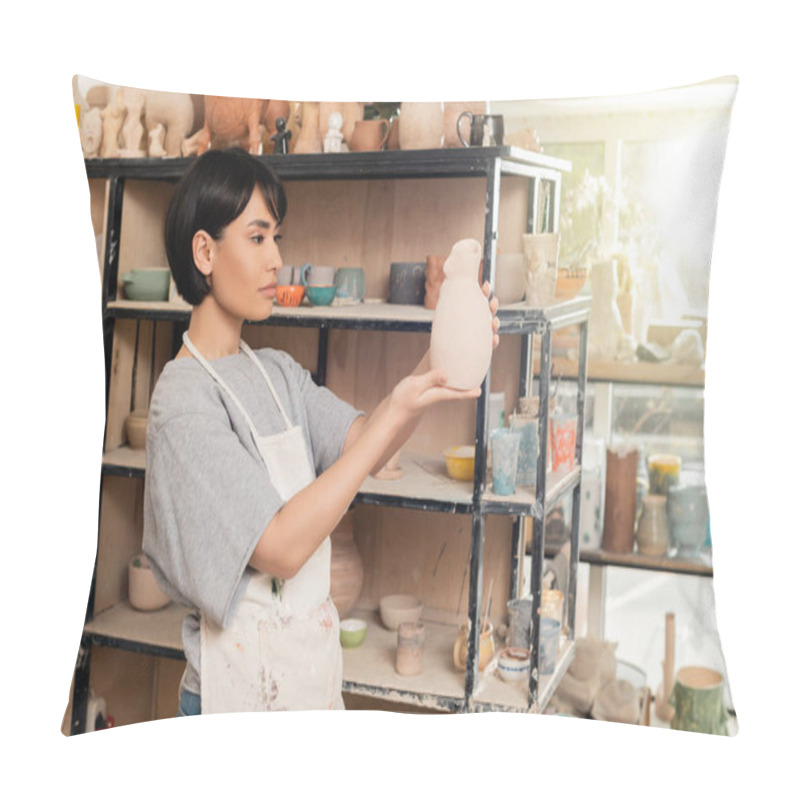 Personality  Young Brunette Asian Female Artisan In Apron Holding Clay Sculpture Near Rack With Shelves In Blurred Ceramic Workshop At Background At Sunset, Artisan Creating Unique Pottery Pieces Pillow Covers